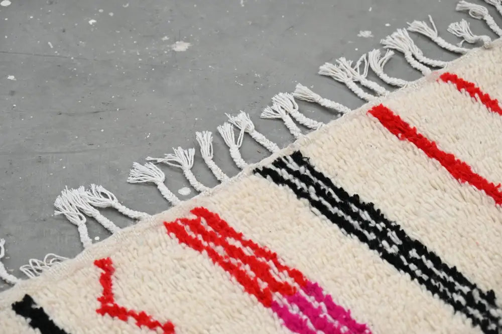 Cream-colored handmade traditional azilal rug with bold red black and pink geometric stripes and white fringe 253x144 cm