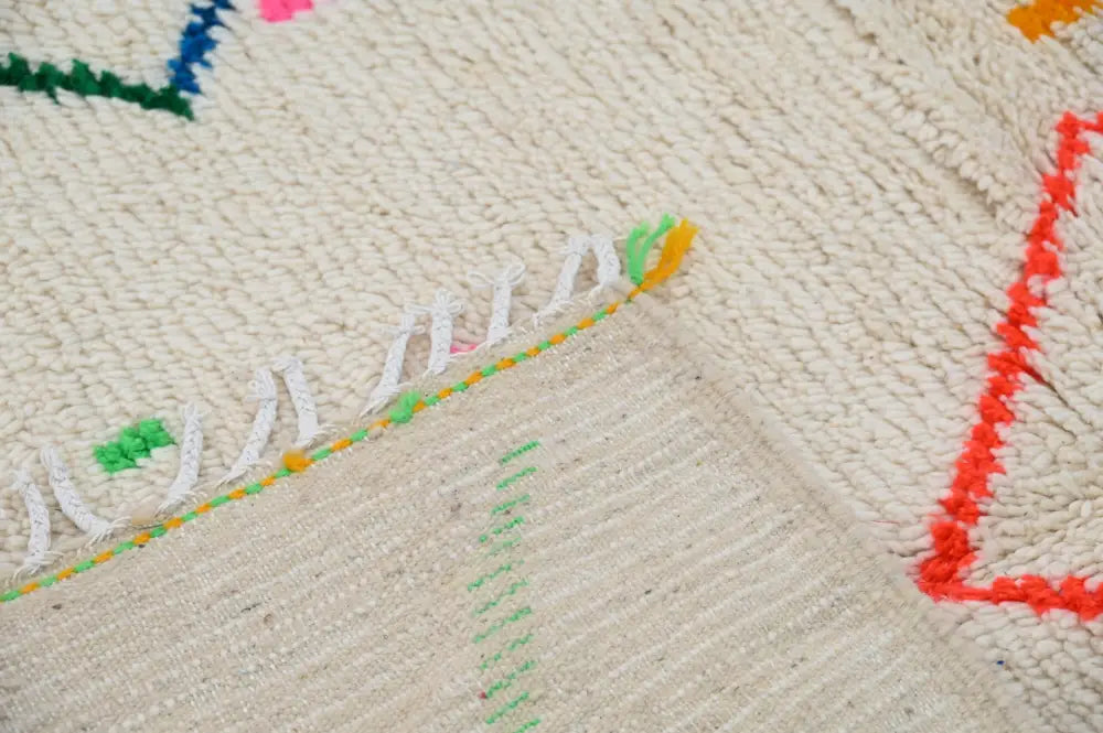 Cream-colored moroccan azilal rug with colorful geometric patterns and fringed edges made of natural wool by DecorBites