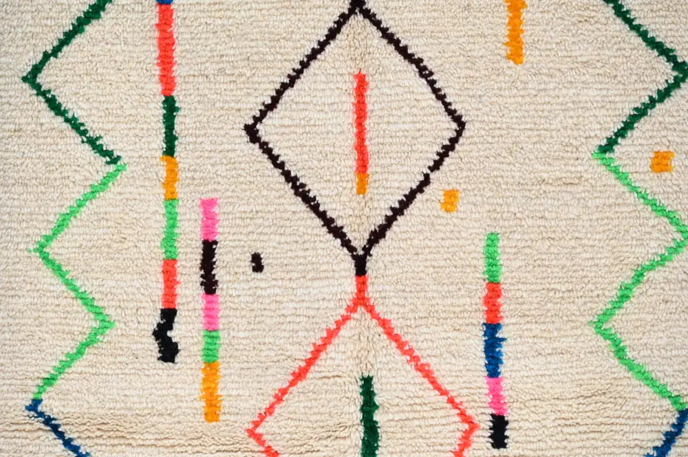 Cream-colored moroccan azilal rug with bold geometric patterns in black red green orange pink and blue made of natural wool