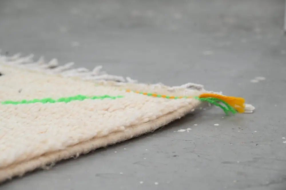 Off-white textured moroccan azilal rug with frayed edge and decorative green stitching made of natural wool
