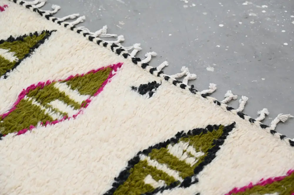 Cream-colored handmade moroccan azilal rug with bold green and magenta geometric patterns and black-and-white fringe