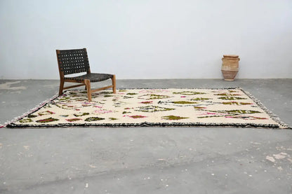 Cream-colored handmade moroccan azilal rug with geometric botanical patterns in muted greens pinks and browns with black fringe