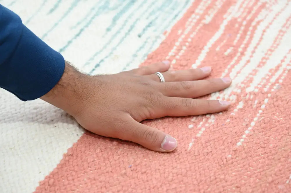A hand with a silver ring rests on a pink and white striped handmade moroccan azilal rug 302x197cm textured surface