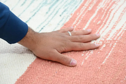 A hand with a silver ring rests on a pink and white striped handmade moroccan azilal rug 302x197cm textured surface