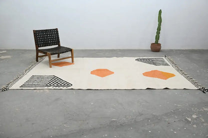 Cream-colored handmade moroccan azilal rug with bold orange hexagons and black geometric patterns with fringed edges