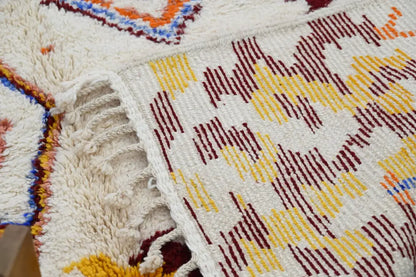 A cream-colored handmade moroccan azilal rug with maroon yellow and blue geometric threads 309x207cm
