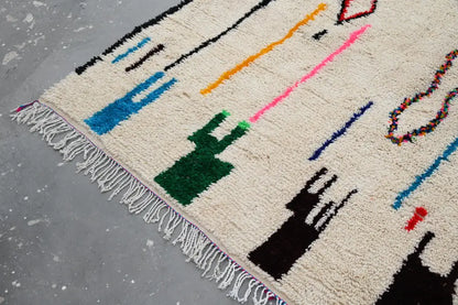 Cream-colored moroccan azilal rug with bold black blue green orange pink red geometric patterns and fringed edge 313x194cm