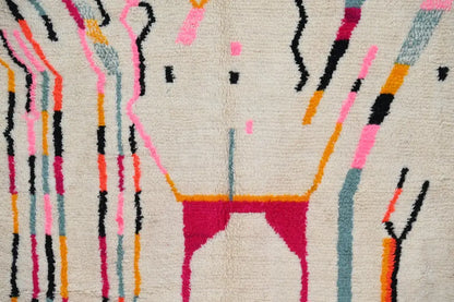 A cream-colored handmade moroccan azilal rug with bold abstract geometric patterns in pink, magenta, black, orange, and teal