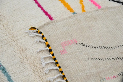 Cream-colored handmade moroccan azilal rug with vibrant pink yellow and black geometric patterns and fringed edge