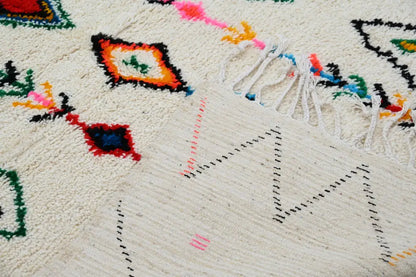Cream-colored decorbites™ handmade traditional azilal rug with vibrant geometric patterns and fringed edges 240x150cm