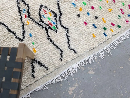 Cream-colored decorbites™ handwoven moroccan azilal rug with black geometric patterns and colorful embroidered dots