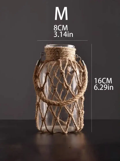 A clear glass hanging vase with woven jute netting and metal clasps featuring hemp rope for rustic decor