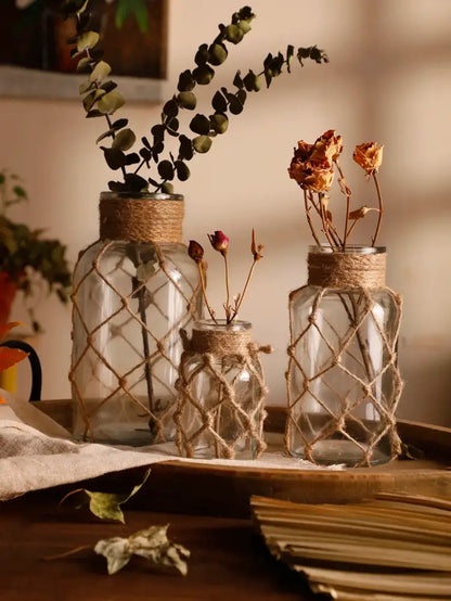 Three clear glass hanging vases wrapped with rustic hemp rope holding dried botanicals for home decor