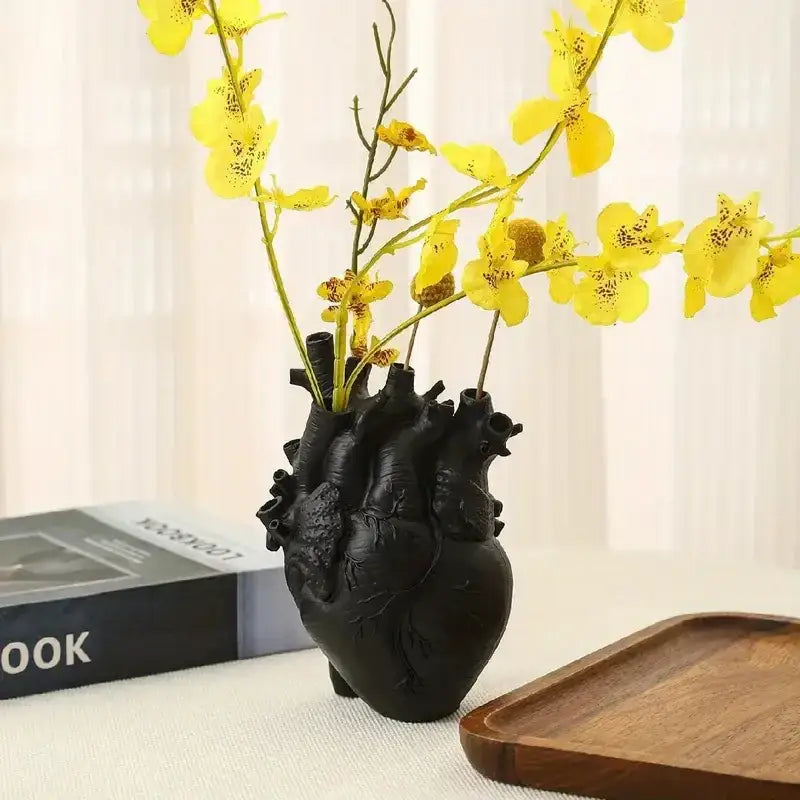 Black DecorBites heart shape resin vase holding yellow orchids showcasing detailed anatomical design
