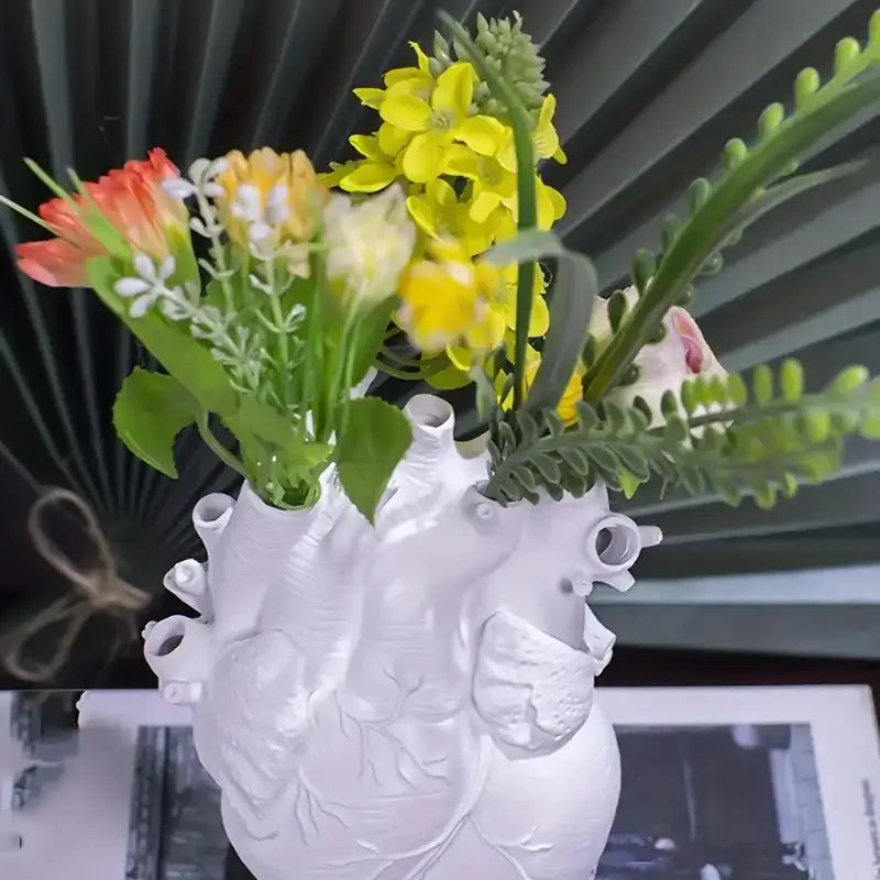 White heart shape resin vase from DecorBites holding yellow, orange, and white artificial flowers bouquet