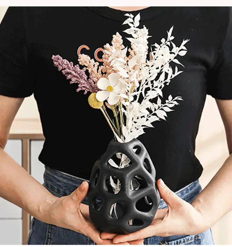 Black ceramic vase with intricate cut-out patterns holding dried flowers in soft pastels nordic classical design