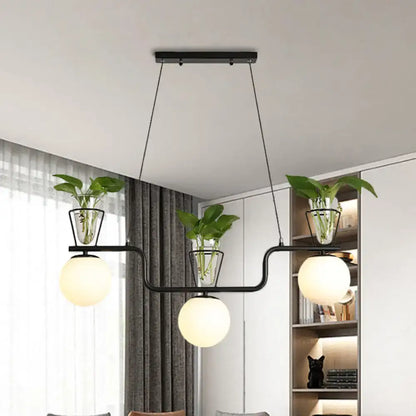 Modern black metal pendant light with three opal glass globes and clear glass pots holding green plants by DecorBites™