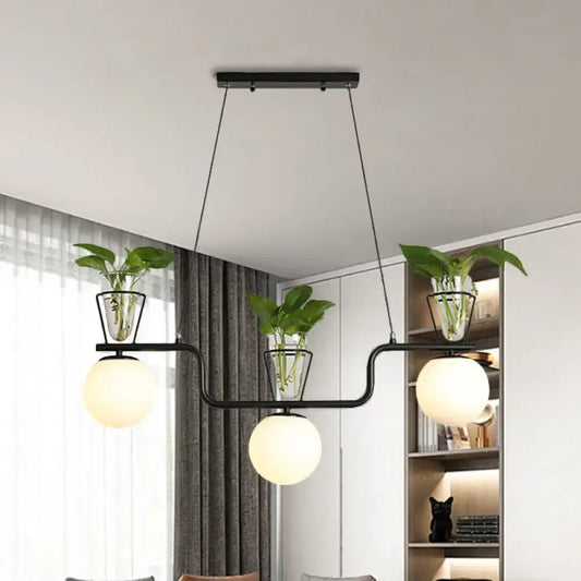 Modern black metal pendant light with three opal glass globes and clear glass pots holding green plants by DecorBites™