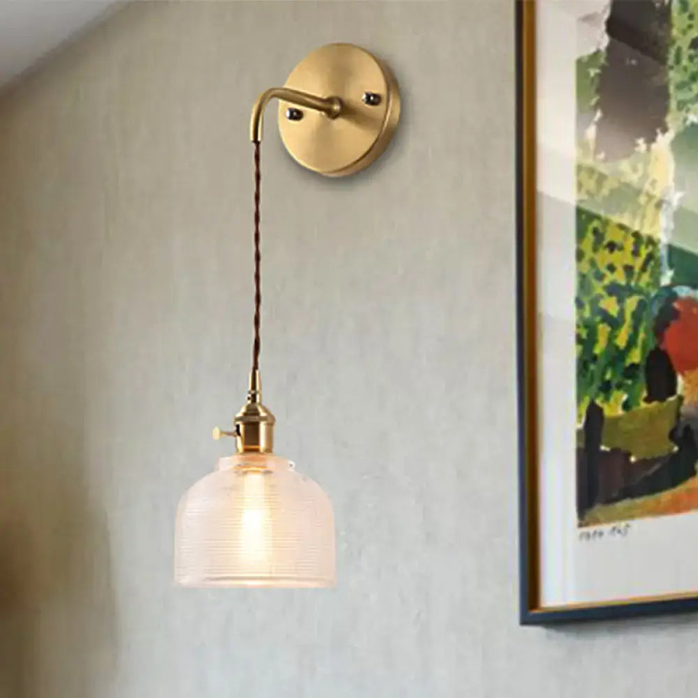 Industrial brass sconce featuring a brass finish with a textured glass dome and twisted cord for bedroom lighting