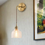 Industrial brass sconce featuring a brass finish with a textured glass dome and twisted cord for bedroom lighting