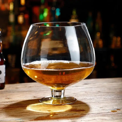 A clear glass decorbites jumbo party snifter filled with amber liquid resting on a wooden dining surface