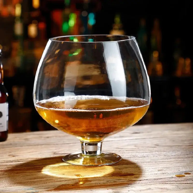 A clear glass decorbites jumbo party snifter filled with amber liquid resting on a wooden dining surface