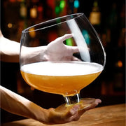 Hand holding a glass of beer with a blurred bar background