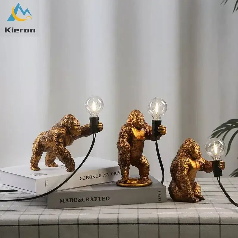Three golden resin gorilla figurines holding lit bulbs on books in decorbites king kong led desk lamp design