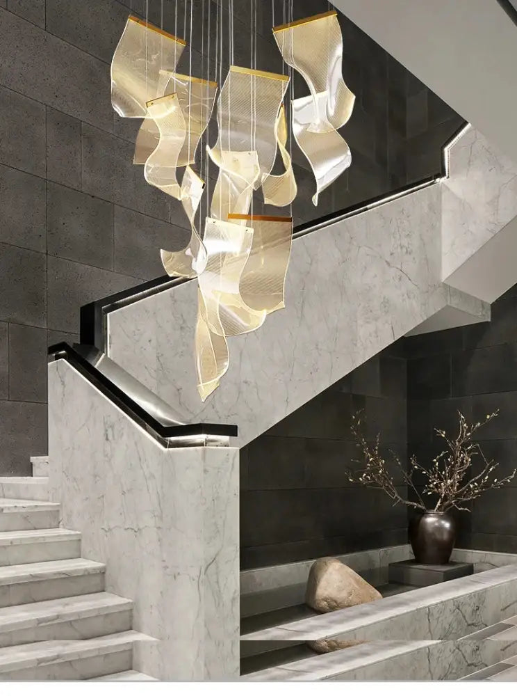 Modern gold-toned metallic led ceiling chandelier with wave-like sculptural elements above marble staircase for living room