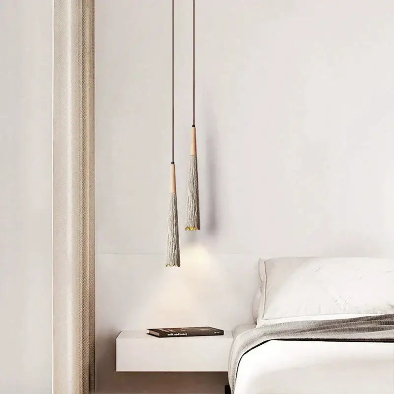 Two minimalist decorbites led cement cream pendant lamps with wooden tops and gray tassels hang above a white table