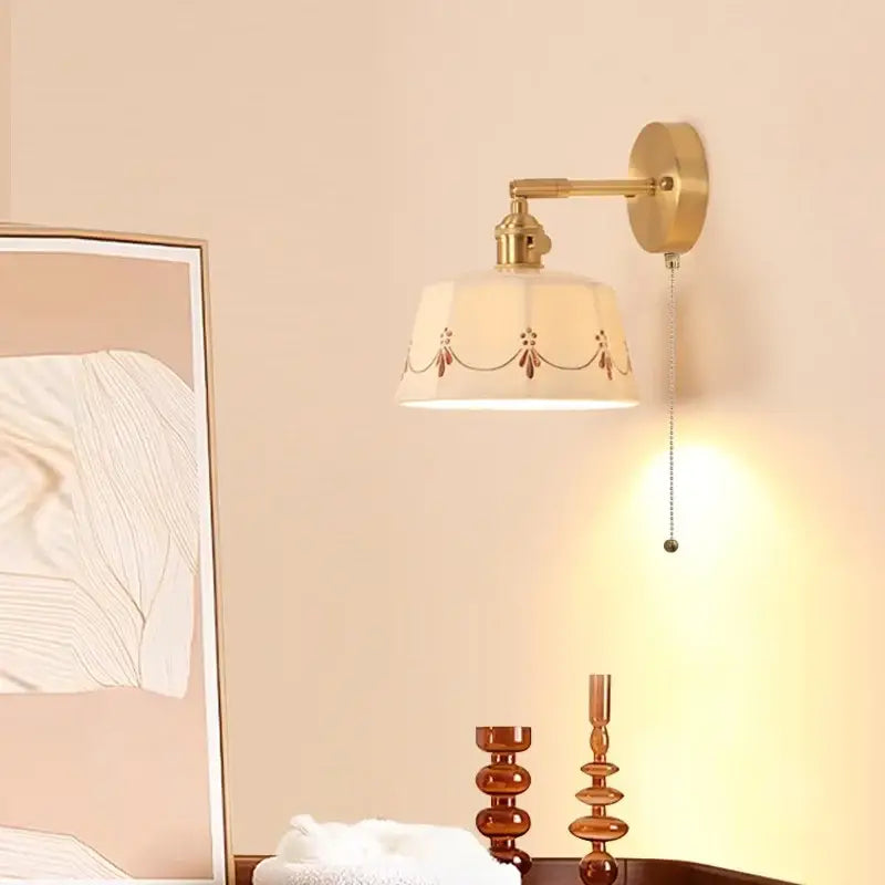 Gold-toned decorbites led ceramic wall lamp with cream fabric shade and brown embroidery featuring pull chain switch