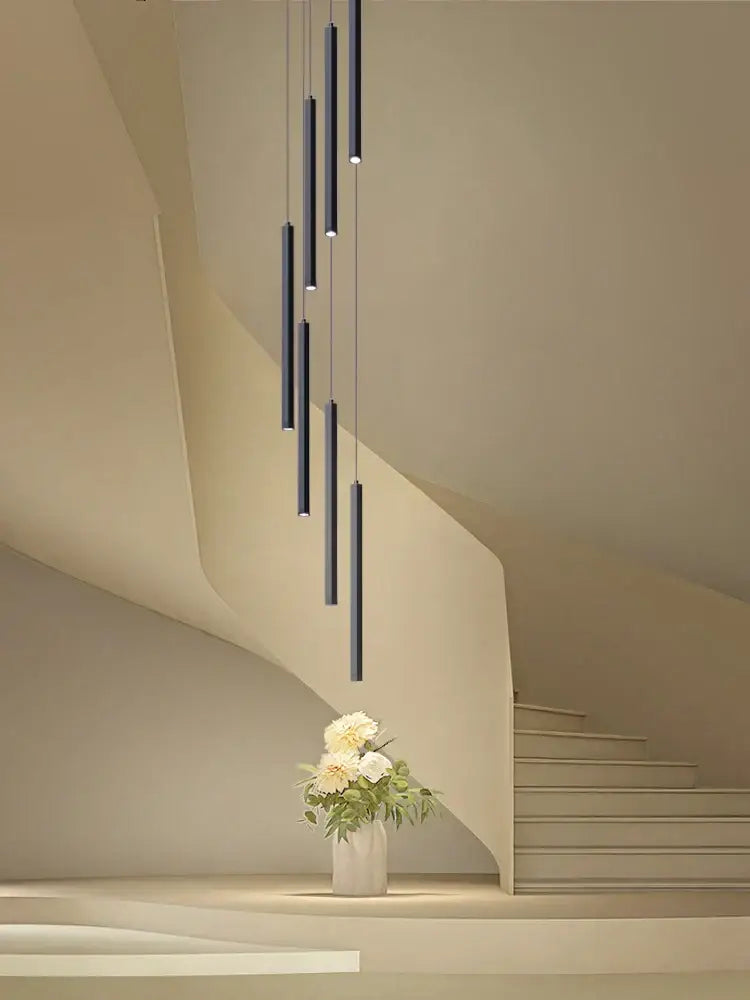Modern black cylindrical decorbites led chandelier stairs pendant lights hang above a white vase with cream flowers