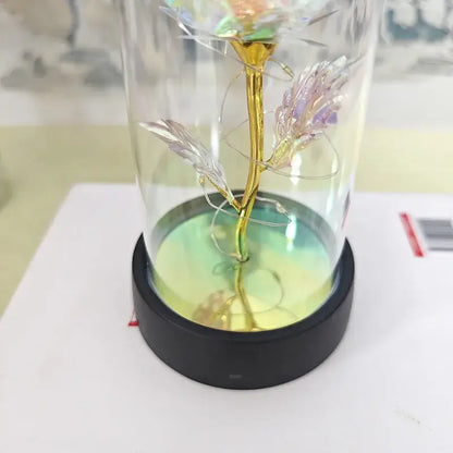 A golden iridescent glass eternal rose light with delicate petals in a clear dome on a black base for weddings