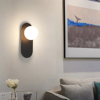 Modern black decorbites led glass ball wall sconce with oval backplate and glowing white spherical bulb for bedroom living room