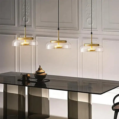 Three elegant gold-toned decorbites led glass bowl pendant lights hang above a sleek black table in a modern setting