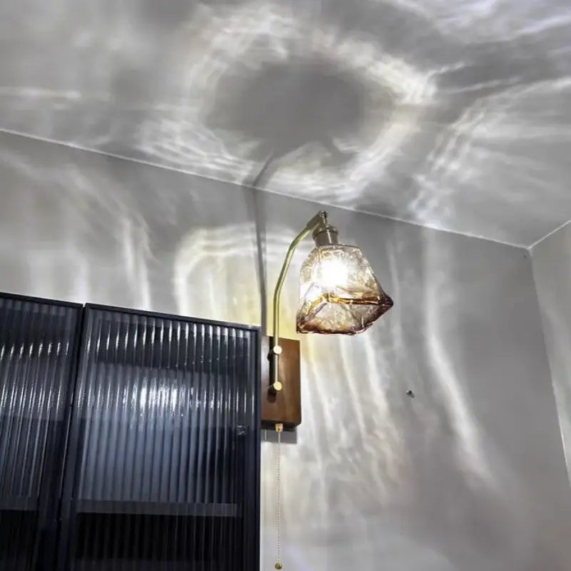 Decorbites™ brass-finished wall sconce with faceted amber glass shade casting swirling light patterns for living room and bedroom