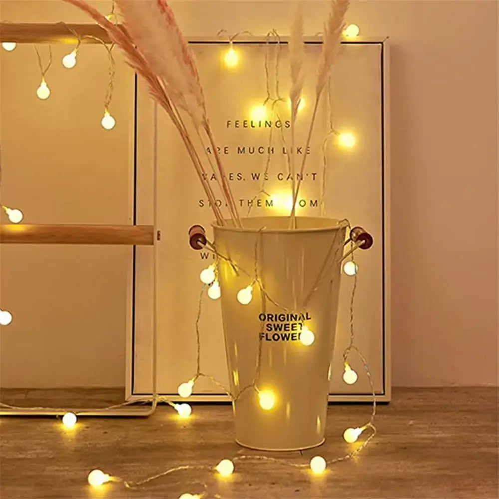 Cream-colored metal bucket with dried pampas grass wrapped in warm white decorbites led globe string lights