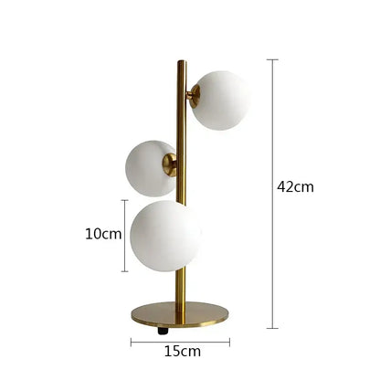 Modern brass table lamp with three milk white glass frosted spherical shades in a vertical cluster by DecorBites