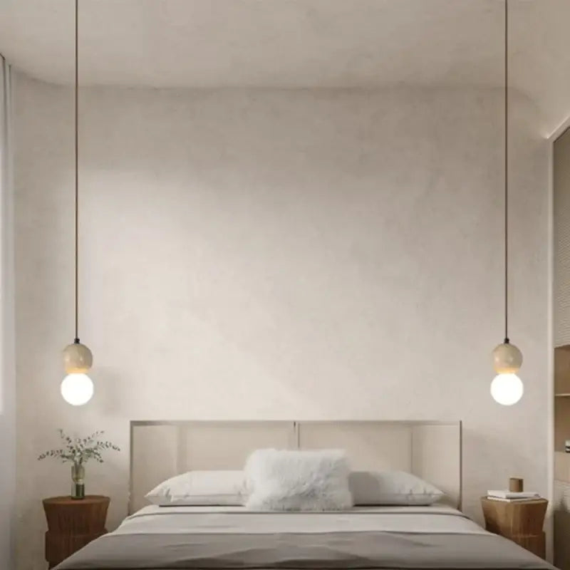 Two decorbites led gourd pendant lights with spherical glass shades and black cords hang symmetrically above a bed