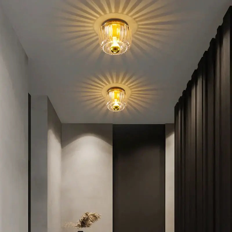 Two elegant gold-toned decorbites led indoor glass wall sconces with clear glass shades casting warm sunburst light patterns