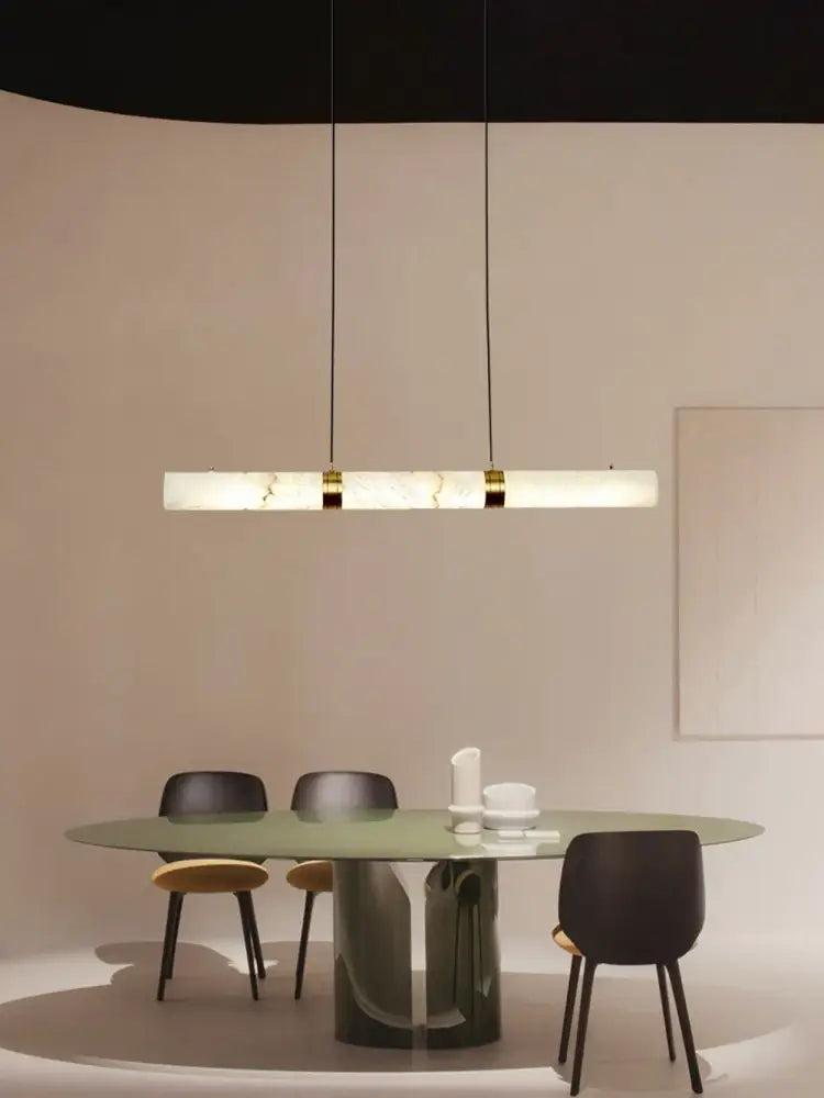 A sleek rectangular led marble hanging lamp in white alabaster with gold accents hanging above a dining table