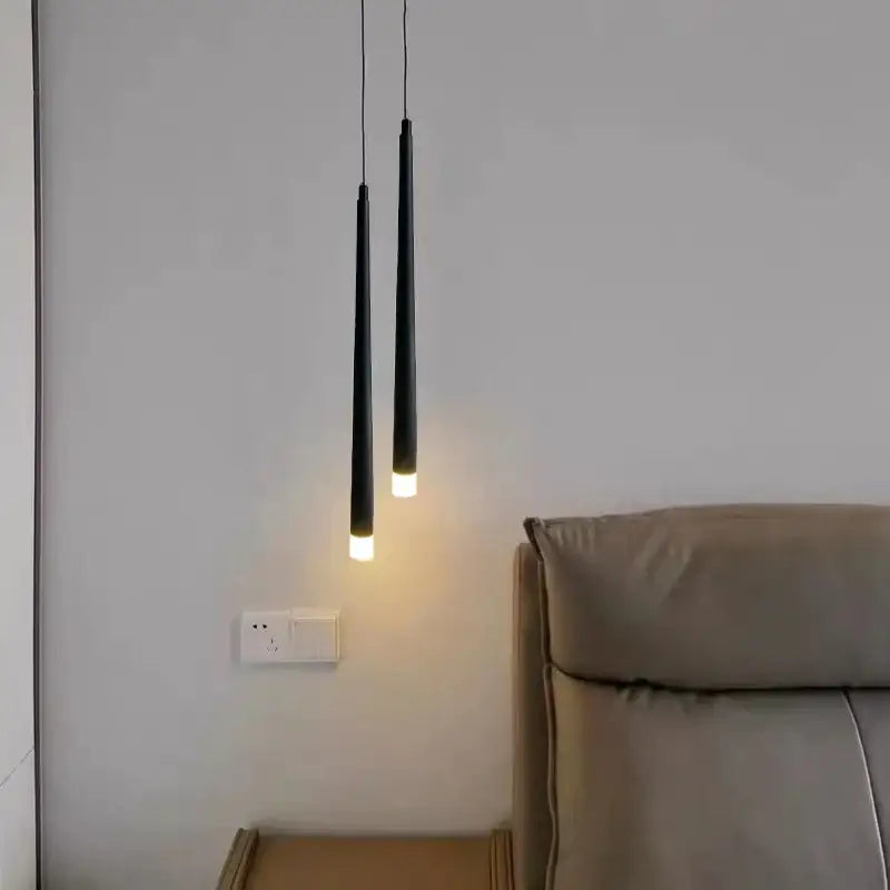 Two sleek black DecorBites LED minimalist pendant lamps with warm bulbs hang above a beige leather headboard