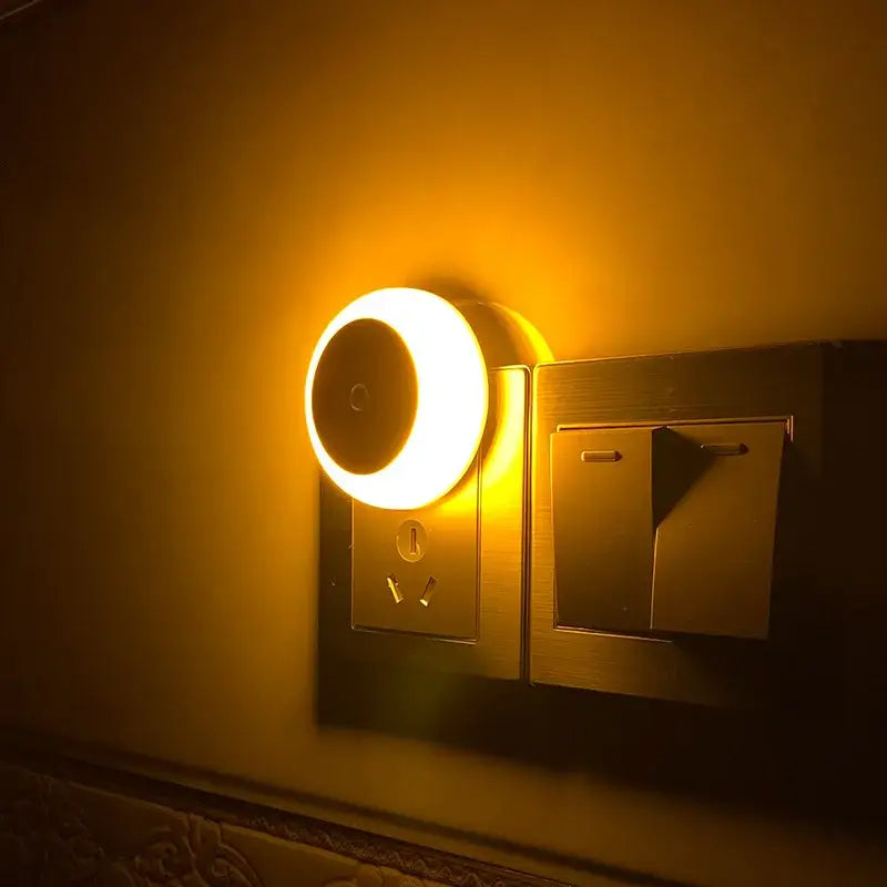 Warm circular DecorBites LED night light with smart sensor and smooth plastic body beside electrical outlet