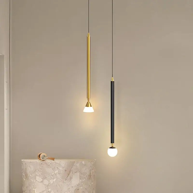 Two minimalist decorbites led pendant lights with gold and black finishes featuring sleek cylindrical bodies and warm globe bulbs