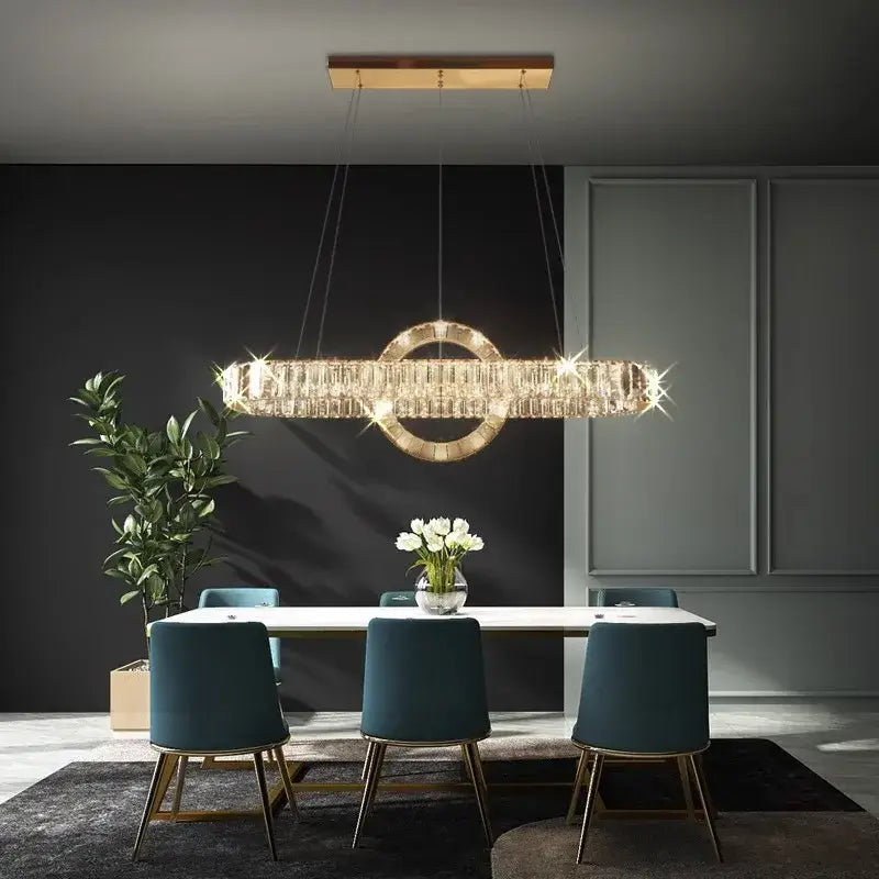 A modern gold-toned decorbites led pendant light chandelier with crystal accents hangs above a dining table