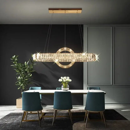 A modern gold-toned decorbites led pendant light chandelier with crystal accents hangs above a dining table