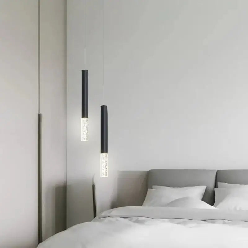 Two sleek black DecorBites LED pendant lights with frosted glass accents hang above a bed in a living room