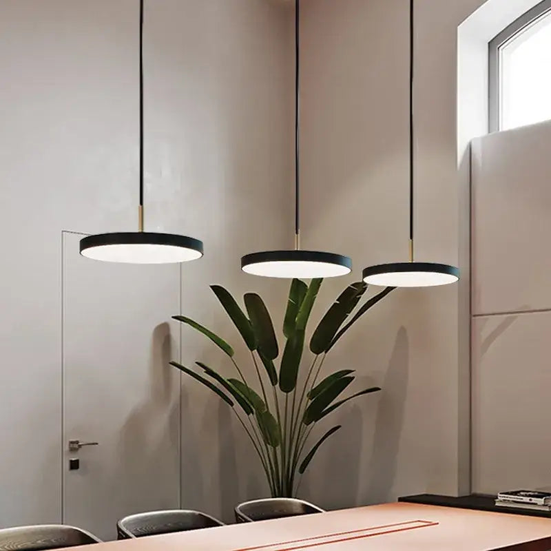 Three decorbites led pendant lights with black iron circular shades hang above a dining table for indoor use