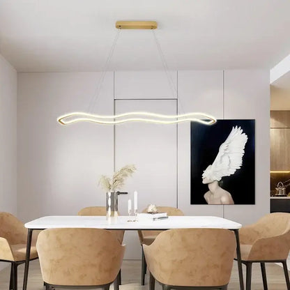 Modern gold-toned aluminum decorbites led pendant light with sleek wavy design hanging above dining table chandelier
