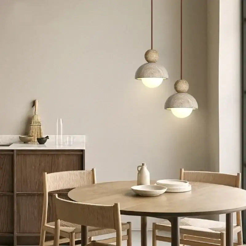 Two minimalist decorbites led pendant lights with textured concrete shades and warm bulbs hang above a wooden table